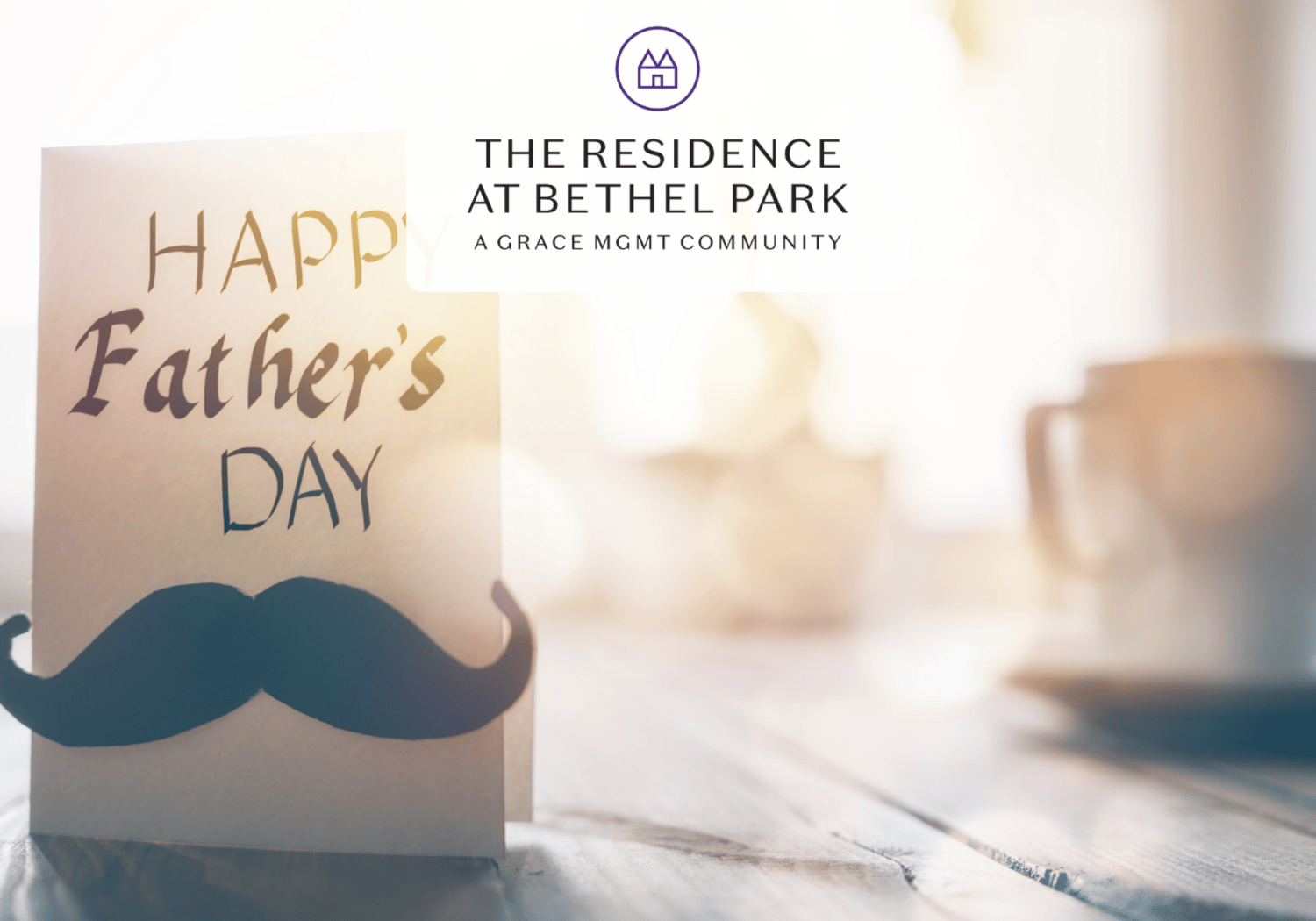 Beige Father's Day card with a black mustache silhouette on a wooden table; blurred background and a brand logo at the top center reading 'The Residence at Bethel Park'