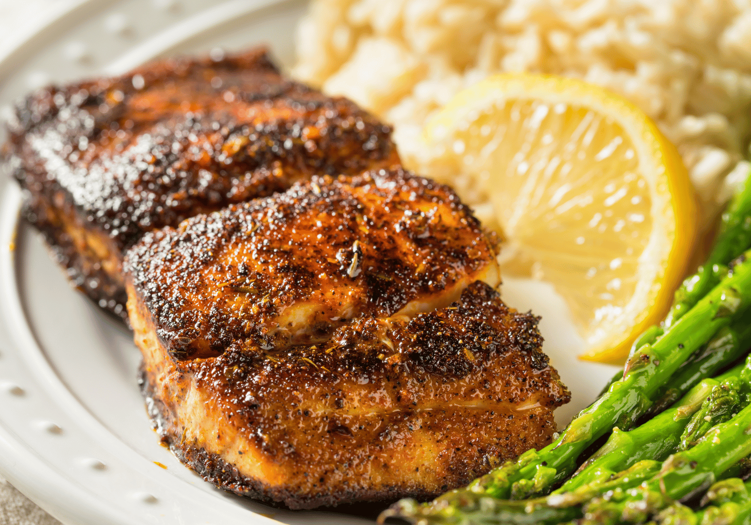 Grilled, herb-crusted chicken breasts with lemon wedge, rice, and asparagus on a plate